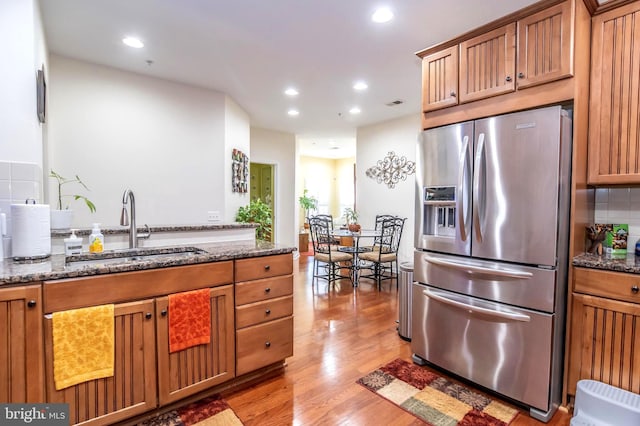 kitchen featuring light wood-type flooring, stainless steel fridge with ice dispenser, sink, and dark stone counters