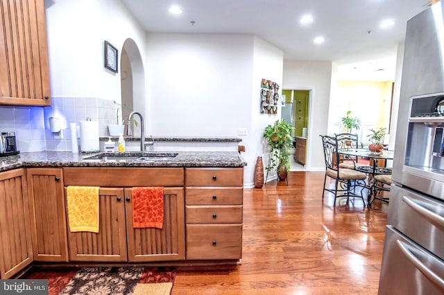 kitchen featuring backsplash, sink, dark stone counters, and stainless steel refrigerator with ice dispenser