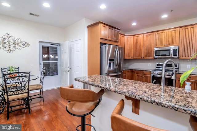 kitchen featuring dark stone counters, dark hardwood / wood-style floors, appliances with stainless steel finishes, tasteful backsplash, and a kitchen bar