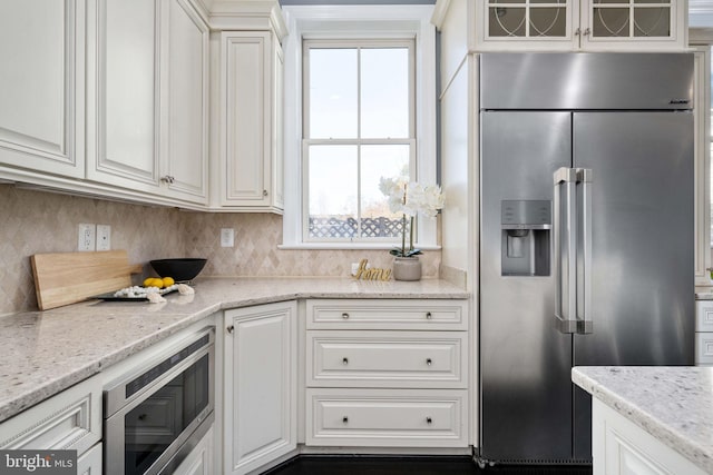 kitchen with built in appliances, white cabinets, light stone counters, and tasteful backsplash