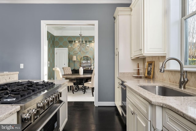 kitchen with hanging light fixtures, sink, stainless steel stove, light stone countertops, and a notable chandelier