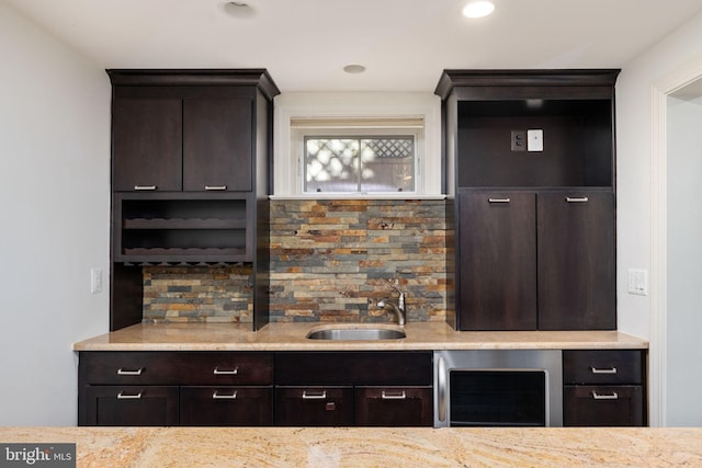 bar featuring wine cooler, dark brown cabinetry, sink, and light stone countertops