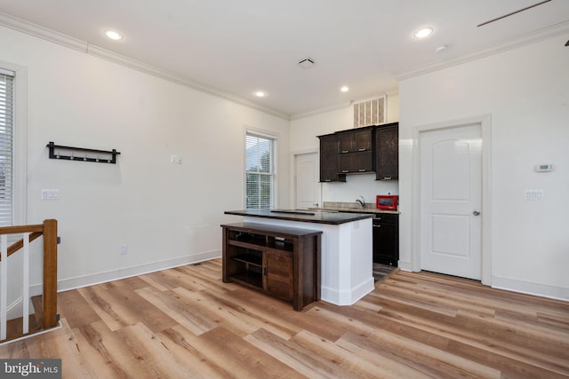 kitchen with light wood-type flooring, dark brown cabinetry, a kitchen island with sink, and ornamental molding