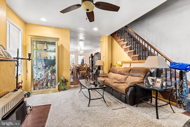 carpeted living room featuring ceiling fan with notable chandelier and heating unit