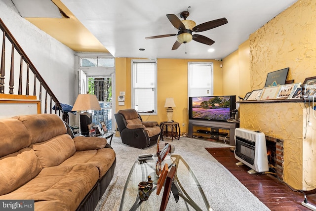 living room featuring ceiling fan, dark carpet, a fireplace, and heating unit