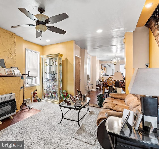 living room featuring wood-type flooring, ceiling fan with notable chandelier, and heating unit