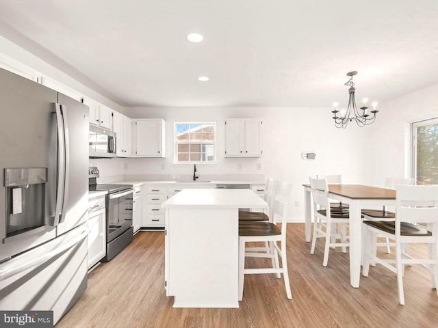 kitchen with stainless steel appliances, a kitchen island, pendant lighting, a chandelier, and white cabinetry