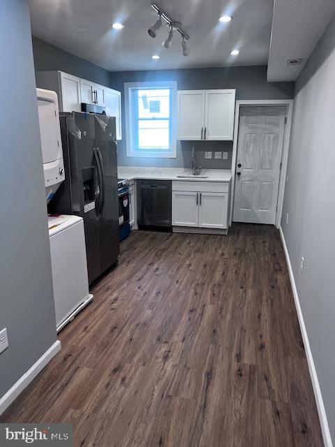 kitchen featuring rail lighting, sink, black appliances, stacked washer / dryer, and white cabinetry