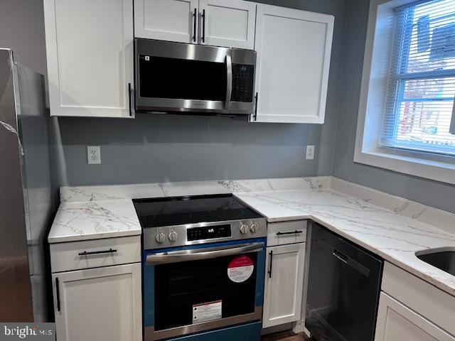 kitchen with light stone counters, white cabinetry, and stainless steel appliances