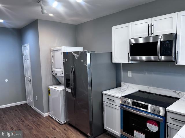 kitchen with light stone countertops, dark hardwood / wood-style flooring, stainless steel appliances, stacked washer / dryer, and white cabinets