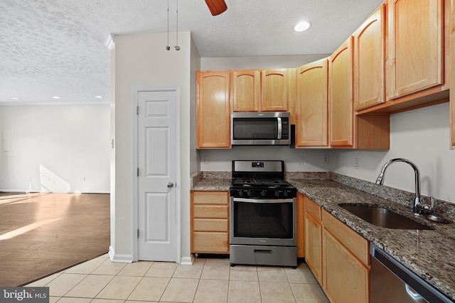 kitchen with stainless steel appliances, sink, light tile patterned floors, and dark stone counters