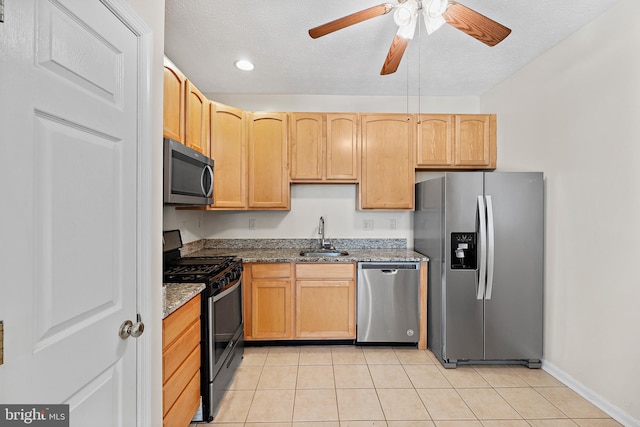 kitchen featuring stainless steel appliances, sink, ceiling fan, light tile patterned floors, and dark stone counters