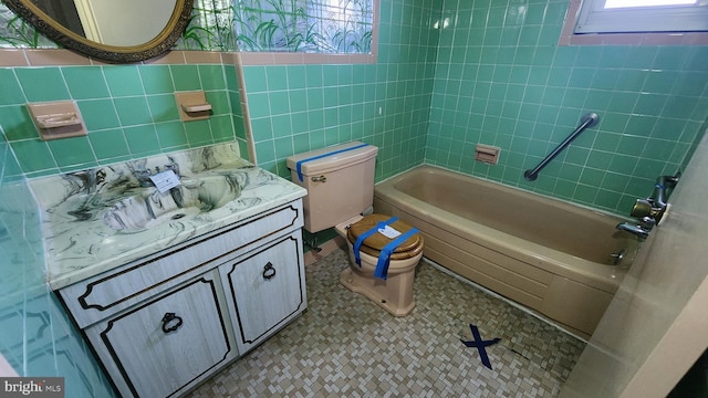 full bathroom with vanity, toilet, tiled shower / bath combo, and tile walls