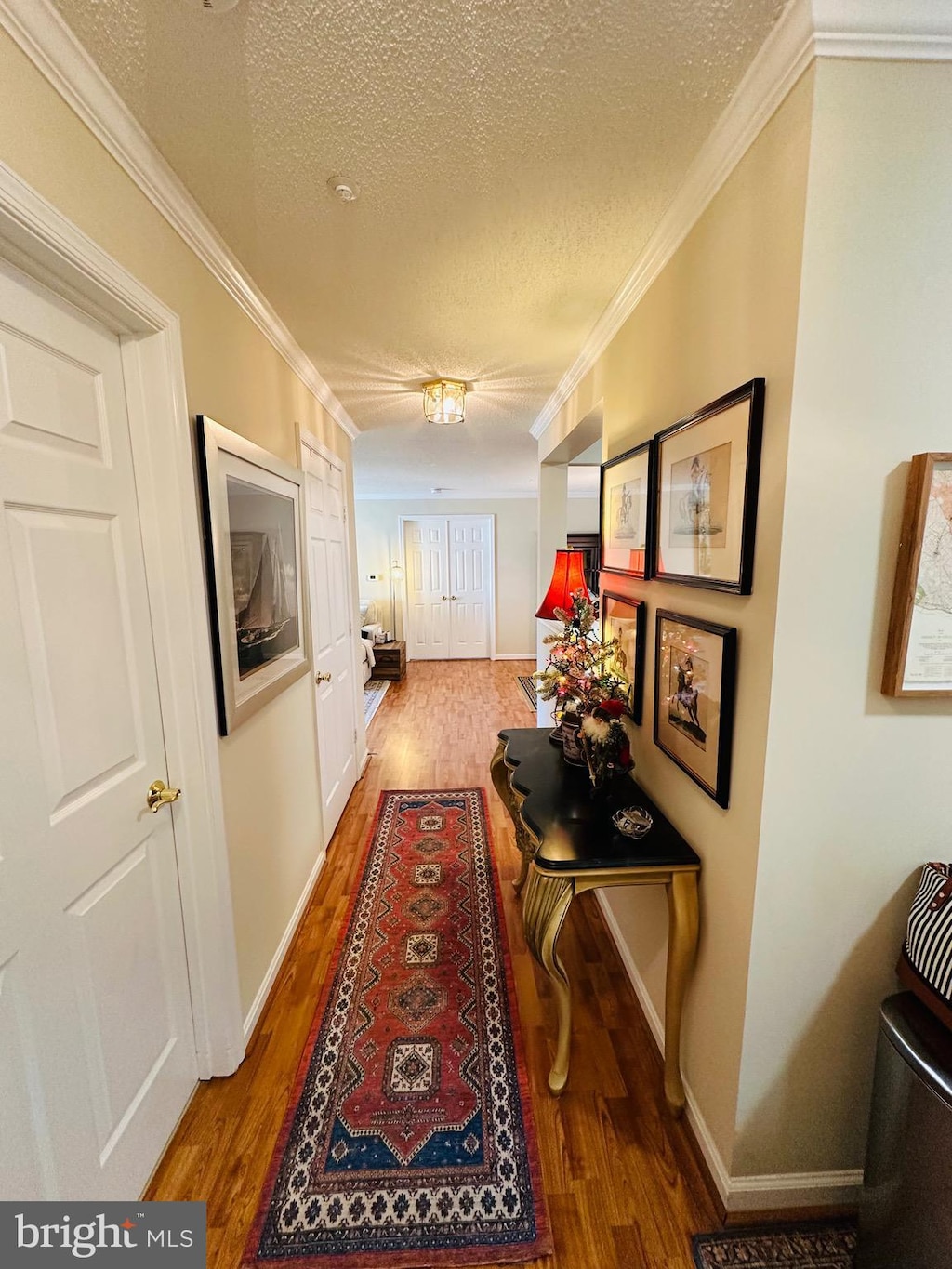 corridor featuring wood-type flooring, a textured ceiling, and ornamental molding