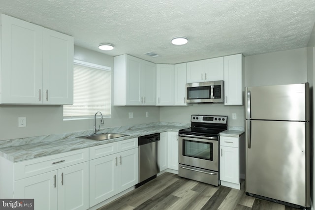 kitchen with light stone countertops, appliances with stainless steel finishes, white cabinetry, and sink