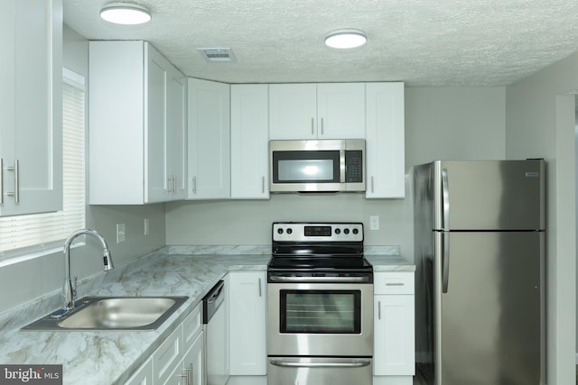 kitchen with light stone counters, sink, white cabinetry, and stainless steel appliances