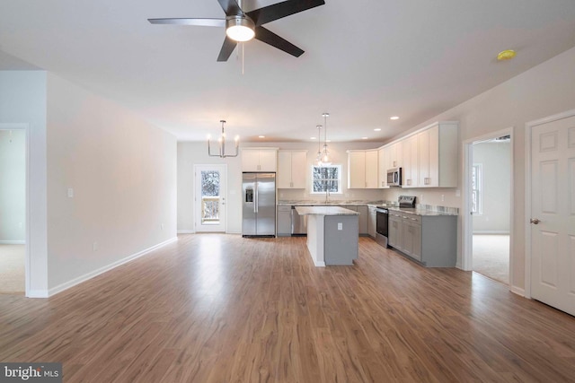 kitchen with light hardwood / wood-style floors, white cabinets, a kitchen island, pendant lighting, and stainless steel appliances