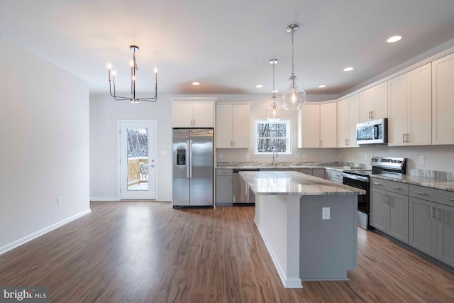 kitchen with gray cabinetry, a kitchen island, decorative light fixtures, stainless steel appliances, and dark hardwood / wood-style floors