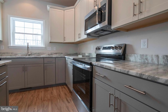 kitchen featuring appliances with stainless steel finishes, sink, white cabinets, light wood-type flooring, and gray cabinetry