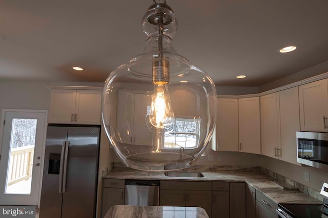 kitchen with hanging light fixtures, sink, white cabinets, light stone counters, and stainless steel appliances