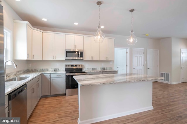 kitchen featuring hanging light fixtures, sink, white cabinetry, a kitchen island, and stainless steel appliances