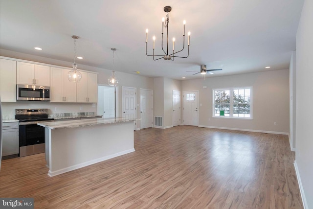 kitchen featuring hanging light fixtures, white cabinetry, light stone counters, a kitchen island, and stainless steel appliances