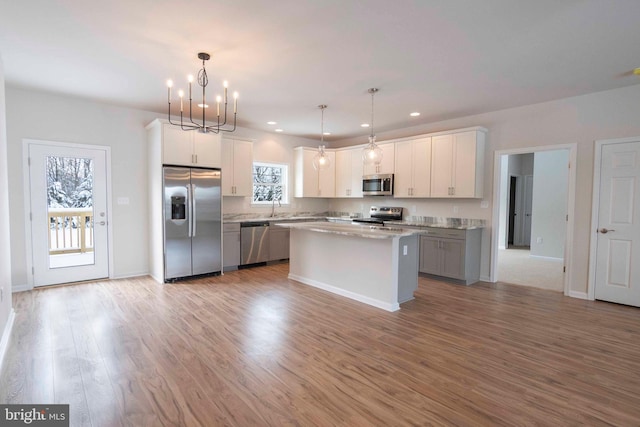 kitchen with decorative light fixtures, sink, white cabinets, a center island, and stainless steel appliances