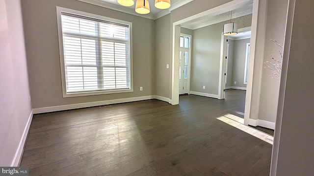 spare room featuring plenty of natural light, ornamental molding, dark wood-type flooring, and an inviting chandelier