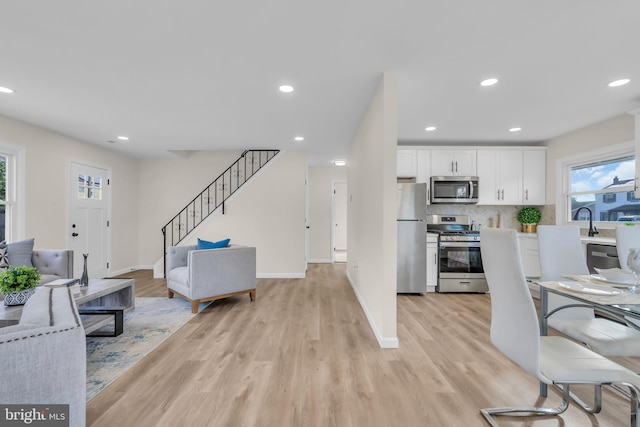 interior space featuring light wood-type flooring, stainless steel appliances, white cabinetry, and tasteful backsplash