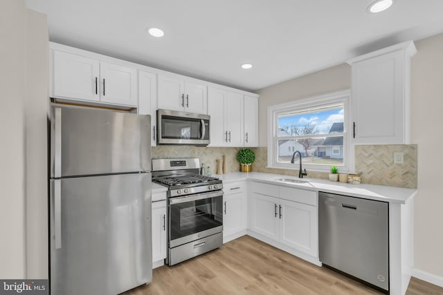 kitchen with decorative backsplash, appliances with stainless steel finishes, sink, light hardwood / wood-style flooring, and white cabinetry