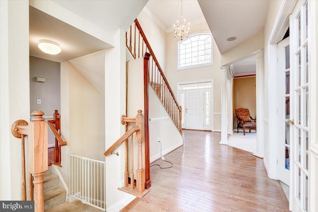 foyer entrance with an inviting chandelier, decorative columns, crown molding, a towering ceiling, and light hardwood / wood-style floors