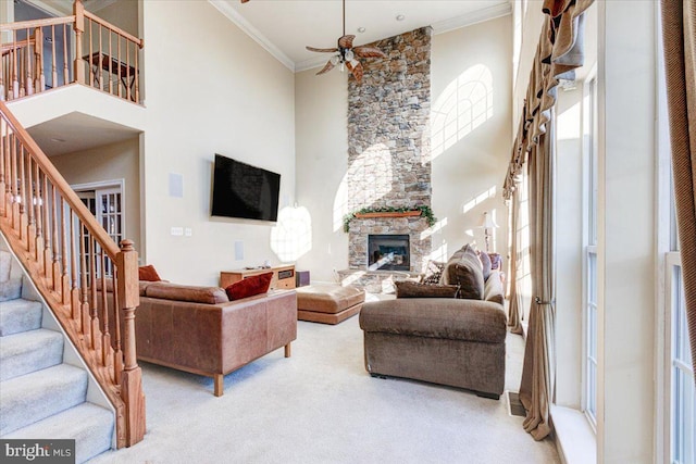 living room featuring ceiling fan, a fireplace, a towering ceiling, and crown molding