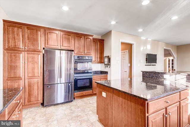 kitchen featuring double oven, a center island, stainless steel refrigerator, and dark stone counters