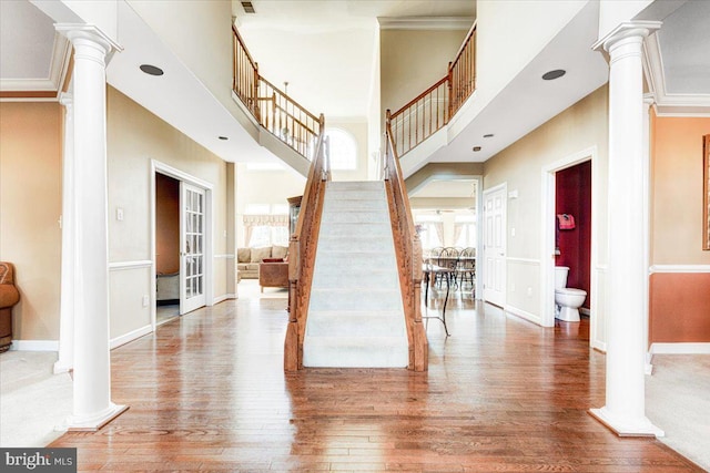 entryway featuring ornate columns, hardwood / wood-style flooring, a high ceiling, and ornamental molding