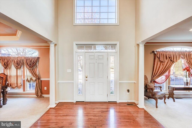 entryway with ornate columns, crown molding, carpet, and a high ceiling