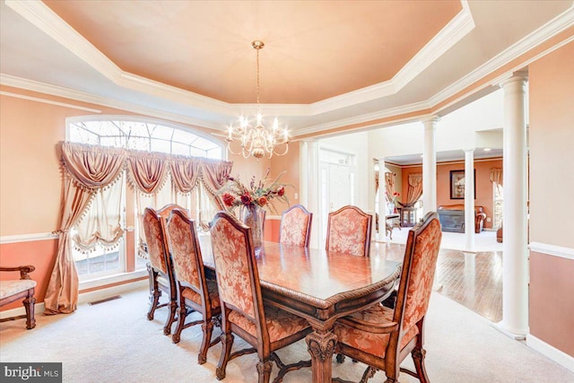 dining room with a chandelier, a raised ceiling, ornate columns, and a healthy amount of sunlight