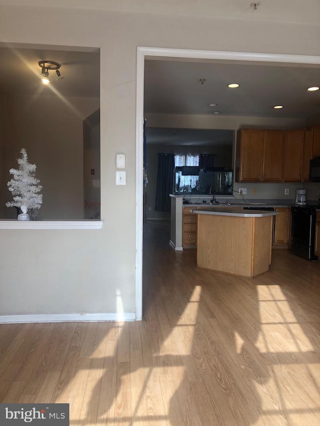 kitchen with sink, black appliances, a center island, and light wood-type flooring