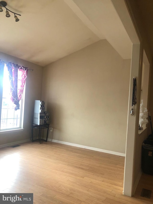 empty room featuring rail lighting, vaulted ceiling, and light hardwood / wood-style flooring