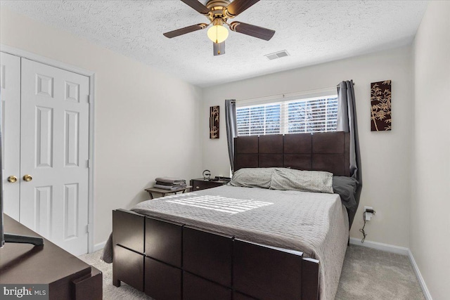 bedroom with a textured ceiling, ceiling fan, light carpet, and a closet