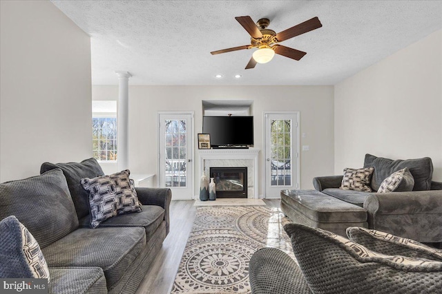 living room featuring a high end fireplace, ornate columns, a textured ceiling, ceiling fan, and light hardwood / wood-style flooring