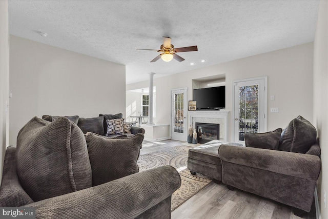 living room with a premium fireplace, ceiling fan, a textured ceiling, and light wood-type flooring