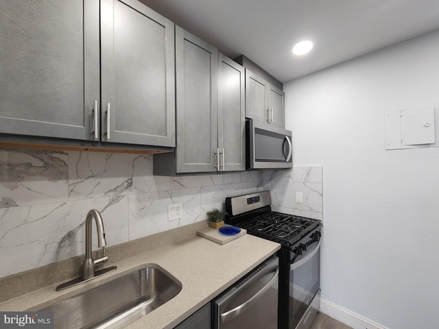 kitchen featuring gray cabinets, sink, backsplash, and appliances with stainless steel finishes