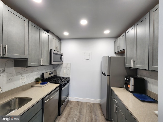 kitchen featuring decorative backsplash, appliances with stainless steel finishes, light hardwood / wood-style floors, and gray cabinets