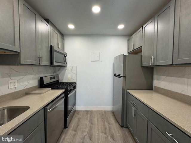 kitchen with gray cabinetry, sink, light wood-type flooring, tasteful backsplash, and stainless steel appliances