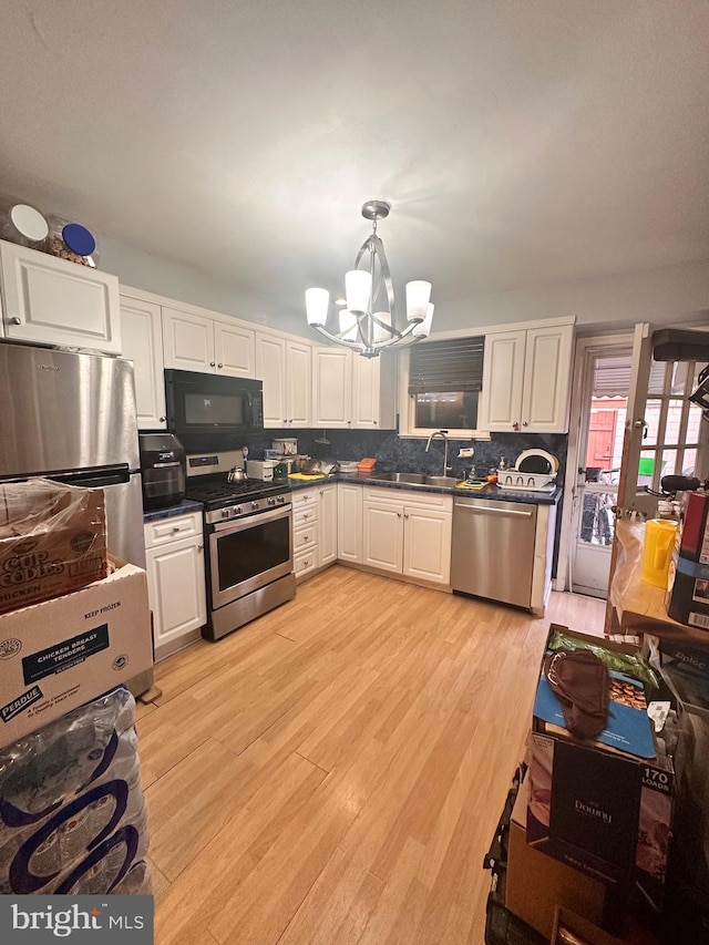 kitchen featuring stainless steel appliances, sink, pendant lighting, a notable chandelier, and white cabinetry