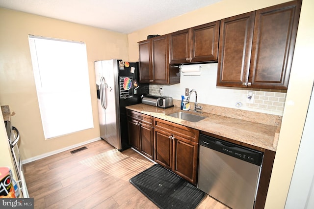 kitchen with backsplash, dark brown cabinetry, stainless steel appliances, sink, and light hardwood / wood-style flooring