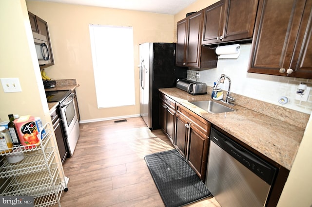 kitchen with dark brown cabinetry, light stone countertops, sink, and appliances with stainless steel finishes