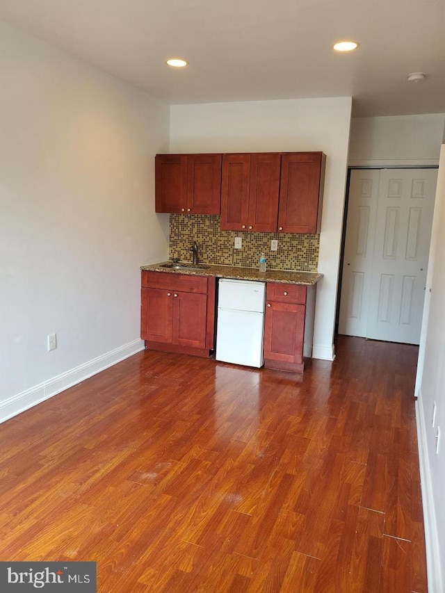 kitchen featuring dark hardwood / wood-style flooring, backsplash, dark stone counters, sink, and dishwasher