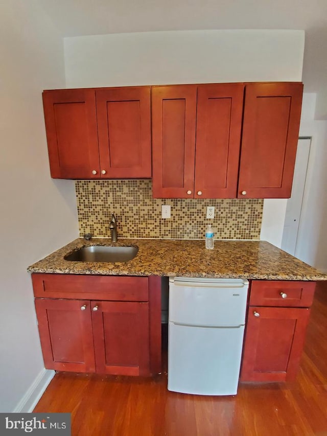 kitchen featuring stone counters, sink, white refrigerator, decorative backsplash, and light wood-type flooring