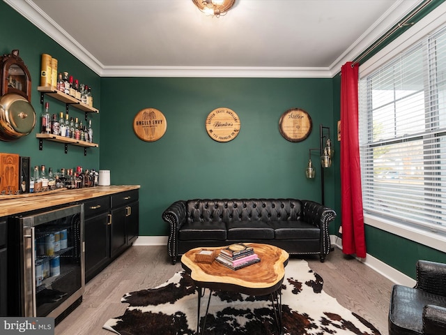 living room featuring light wood-type flooring, crown molding, beverage cooler, and bar area